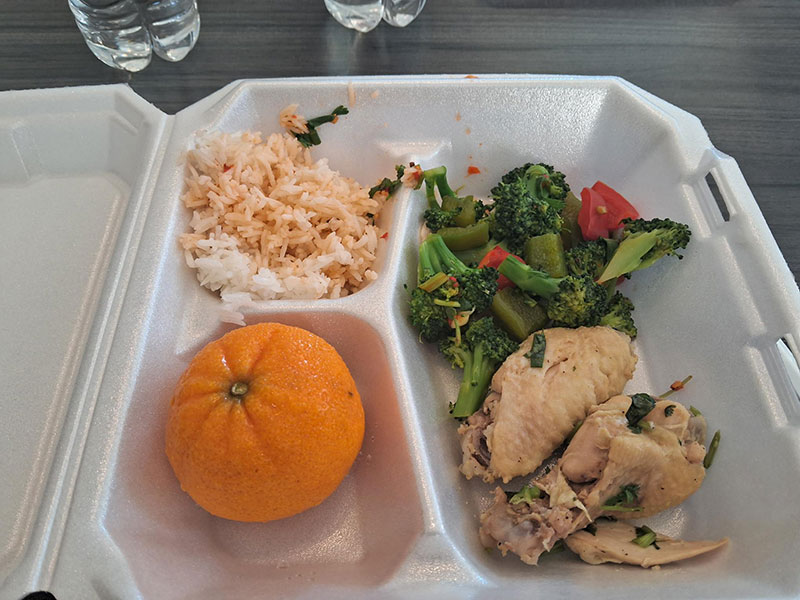 A Hmong lunch in a tray- an orange, rice, chicken and greens