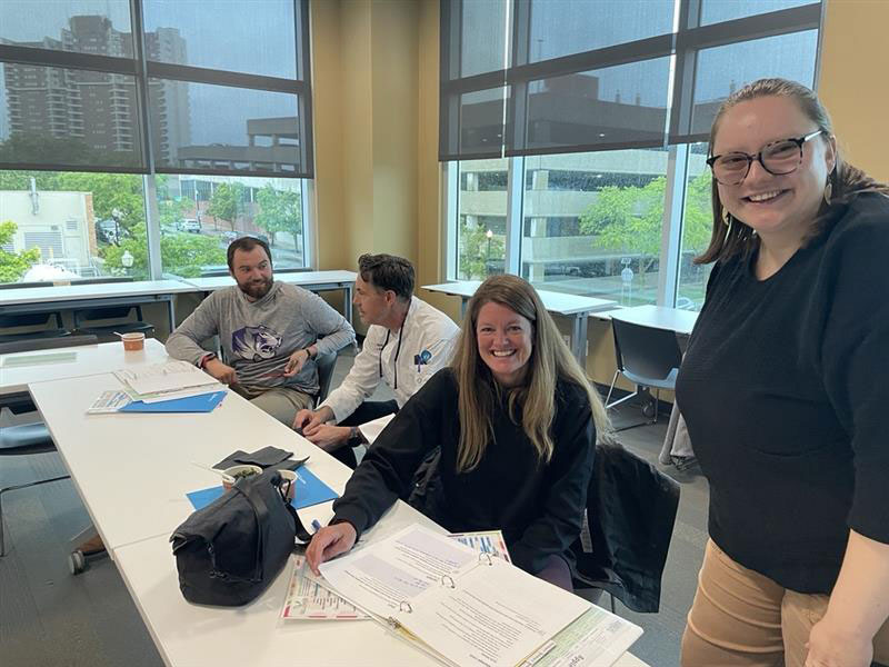 Four people at a long table, looking at the camera