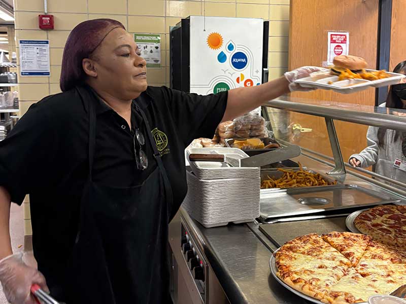 Food service worker handing tray of food to kid in cafeteria.