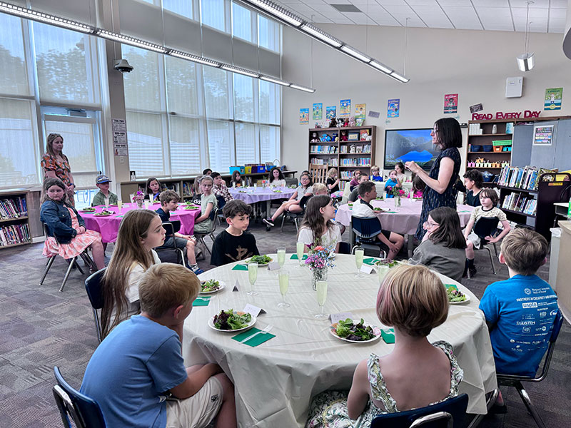 Students sitting at round tables listening to teacher
