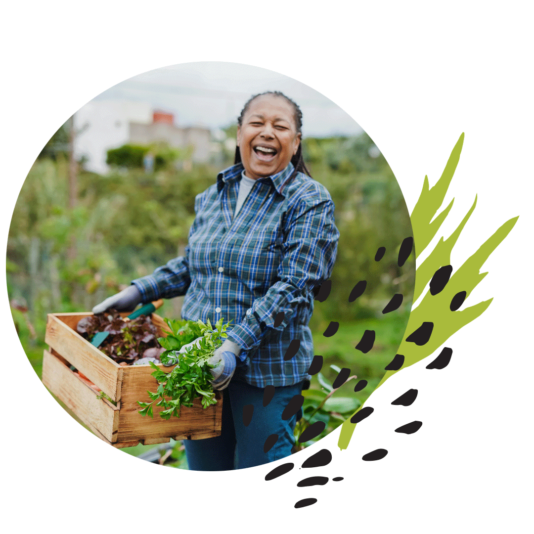 Una mujer sonriente con una camisa a cuadros que sostiene una caja de verduras en un campo
