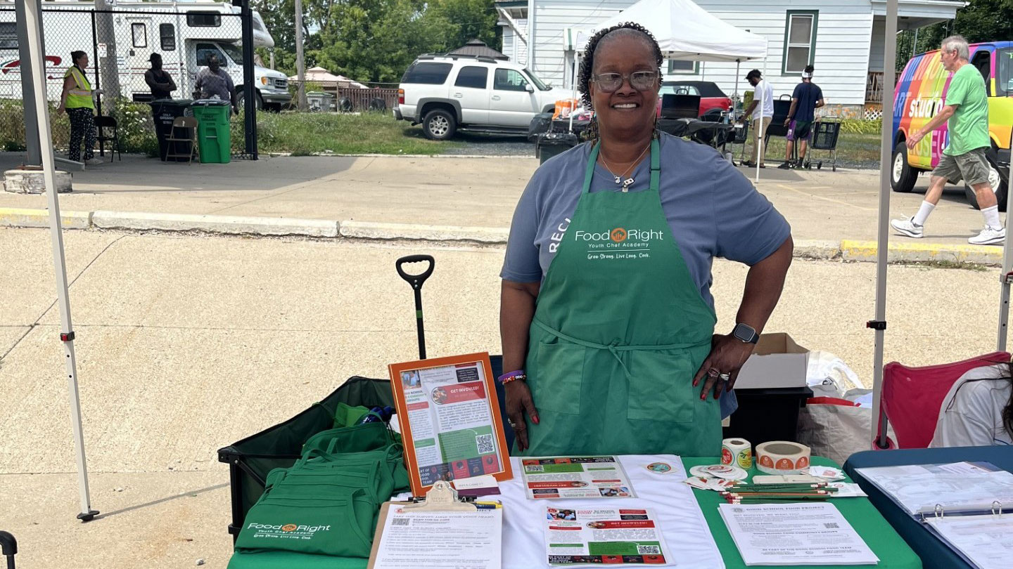 woman in green apron behind table at a community event